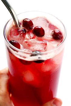 a hand holding a drink with ice and cherries