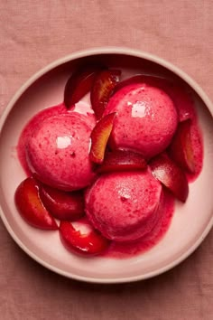 a white bowl filled with red fruit on top of a pink table cloth next to a spoon