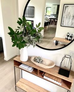 a mirror is hanging on the wall above a table with a vase and plant in it