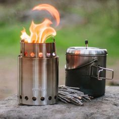 an outdoor stove with flames coming out of it and a pot on the ground next to it