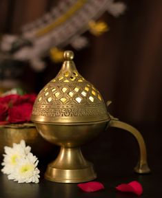 a brass oil lamp next to flowers on a black table with red and white petals