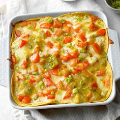 a casserole dish with carrots, green onions and cheese in it on a white cloth