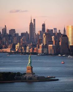 the statue of liberty in new york city is seen from across the water at sunset