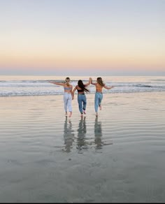 three girls are running on the beach with their arms in the air