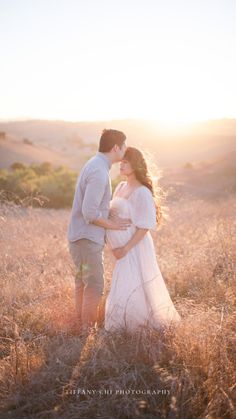 a pregnant couple standing in the middle of a field at sunset