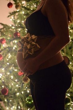 a pregnant woman standing in front of a christmas tree