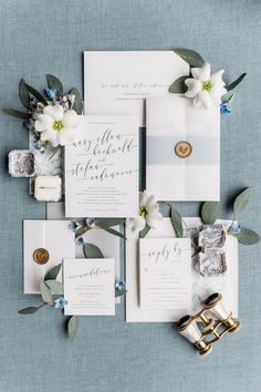 the wedding stationery is laid out on top of each other with white flowers and greenery