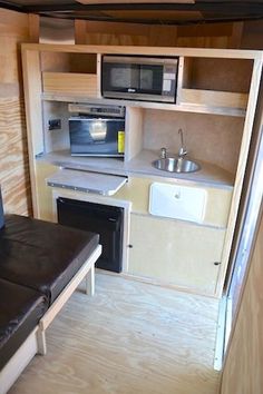 a small kitchen area in a trailer with wood paneling and black leather couches