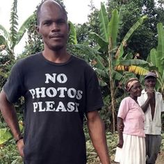 two men standing next to each other in front of trees and banana plants with no photos please written on the t - shirt