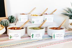 bowls of food on a table with place cards and succulents in them