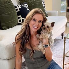 a woman sitting on a couch holding a small dog in her lap and smiling at the camera