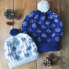 two knitted hats sitting on top of a wooden floor next to pinecones