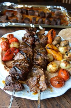 a plate with meat and vegetables on it next to a tray of potatoes, tomatoes and carrots