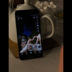 a cell phone sitting on top of a table next to a teapot and cup