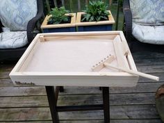 a table with some plants in it on a wooden deck next to two chairs and a potted planter