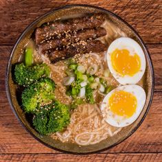 a bowl filled with noodles, meat and broccoli on top of a wooden table