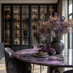 a dining room table with purple chairs and flowers in a vase on the centerpiece