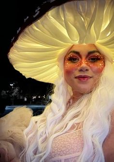 a woman with white hair and makeup wearing a large yellow mushroom hat on top of her head