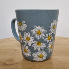 a blue and white coffee cup with daisies painted on the side sitting on a wooden table