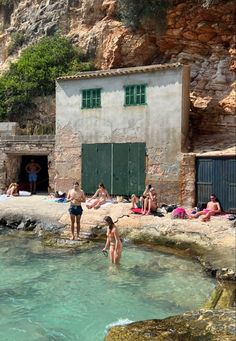 some people are swimming in the water near a building with green shutters and doors