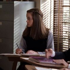 two people sitting at desks with papers and pens in their hands, one person is writing