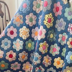 a blue quilt with many different colored flowers on it and a chair in the background