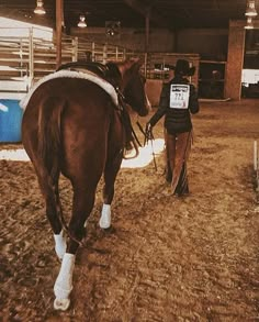 a man leading a horse in an indoor arena