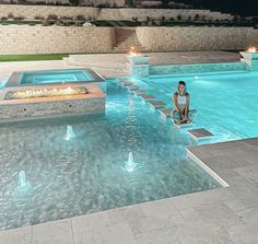 a woman sitting on steps next to a swimming pool with fire pit in the middle