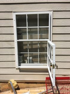 an open window sitting on the side of a house next to a shopping cart and ladder