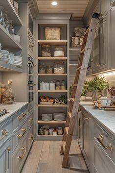 a ladder in the middle of a kitchen with white cupboards and shelves filled with dishes