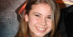 a young woman with long hair smiling at the camera while wearing a black jacket and blue shirt