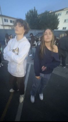 two young people standing next to each other in a parking lot