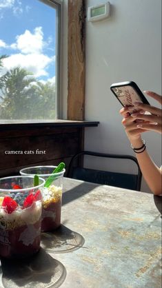 a woman sitting at a table with a cell phone in her hand while looking at the screen