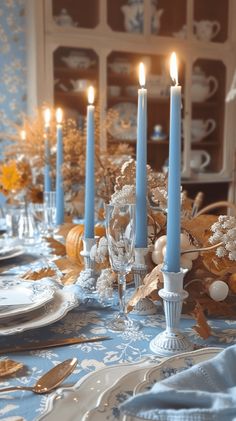 a dining room table is set with blue and white dishes, silverware, and candles