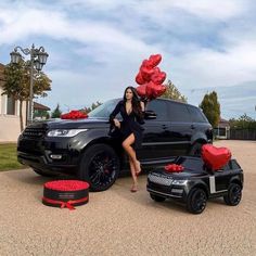 a woman posing next to a black range rover with red balloons