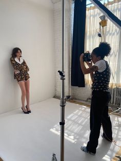 two women standing in front of a white wall taking pictures with their camera and another woman behind them