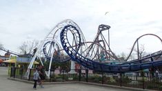 a roller coaster at an amusement park with people walking around the track and onlookers in the background