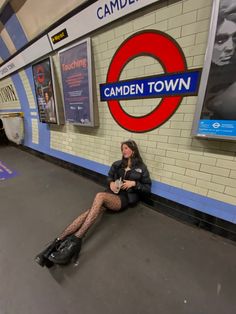 a woman sitting on the ground in front of a train station with her legs crossed