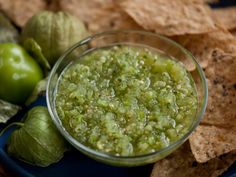 a glass bowl filled with green salsa next to tortilla chips