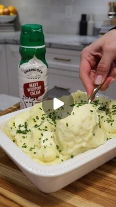 a person cutting up mashed potatoes in a white dish on a wooden counter top