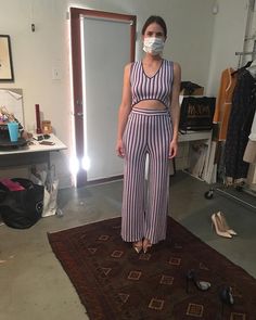 a woman wearing a face mask standing on a rug in a room with clothes and shoes