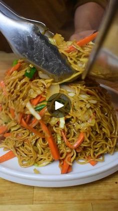 someone is cutting up some noodles on a white plate with carrots and green peppers