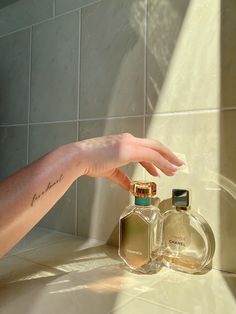 a person's hand reaching for two perfume bottles