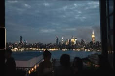 people are sitting at a table in front of a view of the city lights and skyscrapers