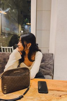 a woman sitting at a table with a purse and cell phone in front of her