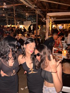 three women in black dresses standing next to each other at a party with people sitting around