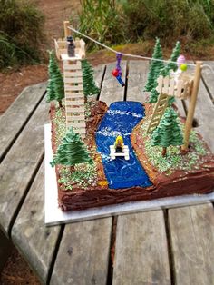 a cake that is sitting on top of a picnic table with trees and a bridge