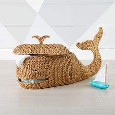 a whale shaped basket sitting on top of a wooden floor next to a toy sailboat