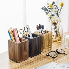 a wooden desk with some pens, pencils and glasses on it next to a vase filled with flowers