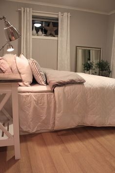 a white bed sitting next to a wooden table with a lamp on top of it